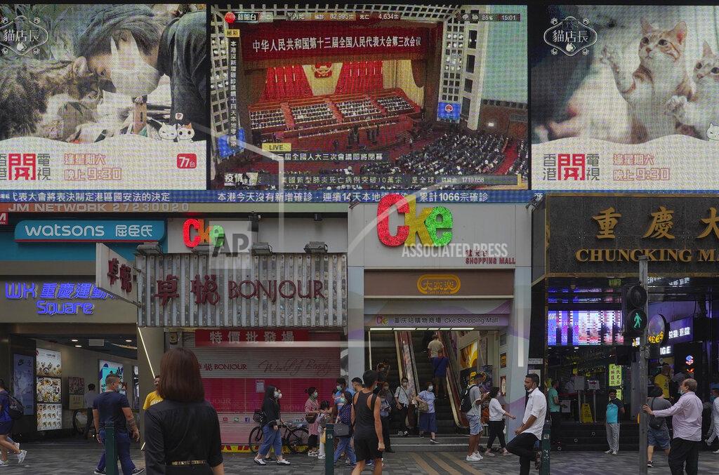 Pedestrians walk under a giant screen showing live telecast of the closing session of the National People's Congress, top center, in Hong Kong, Thursday, May 28, 2020. China’s ceremonial legislature on Thursday endorsed a national security law for Hong Kong that has strained relations with the United States and Britain. (AP Photo/Vincent Yu)