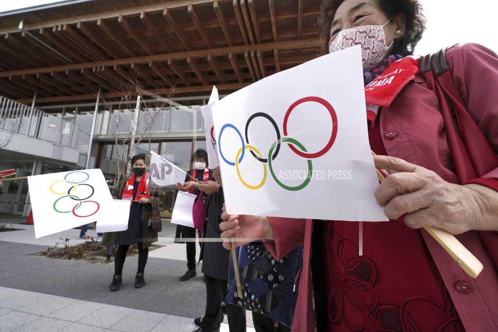 Eugene Hoshiko Local residents carry handmade flags featuring Olympic Rings at the torch relay route of the first section of the Fukushima Torch Relay in Naraha, Fukushima prefecture, northeastern Japan, Thursday, March 25, 2021. The torch relay for the postponed Tokyo Olympics began its 121-day journey across Japan on Thursday and is headed toward the opening ceremony in Tokyo on July 23. (AP Photo/Eugene Hoshiko)