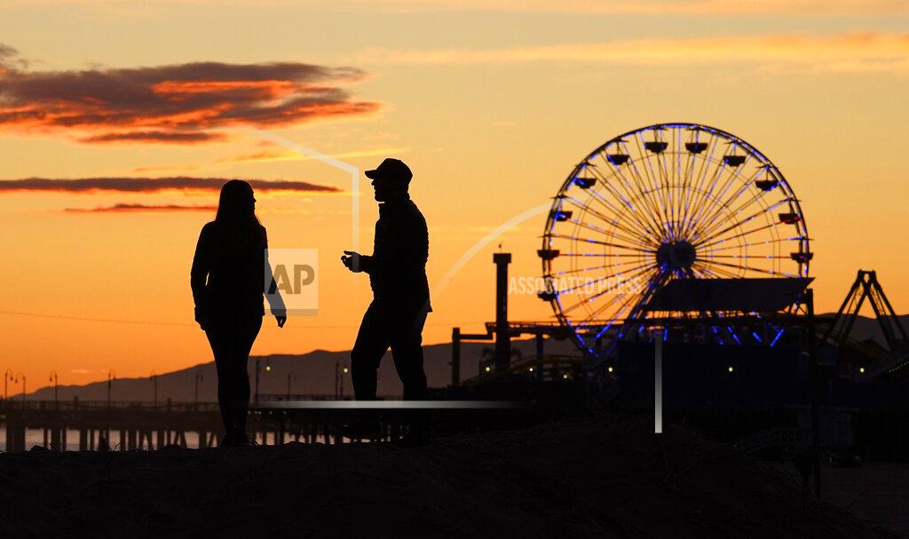 Mark J. Terrill A couple takes photos as the Ferris wheel on Santa Monica pier is lit up in blue on Santa Monica State Beach, Friday, April 10, 2020, in Santa Monica, Calif. The landmark and several others around Los Angeles and the nation are lit up blue to show support for medical workers and first responders on the front lines of the coronavirus pandemic. (AP Photo/Mark J. Terrill)