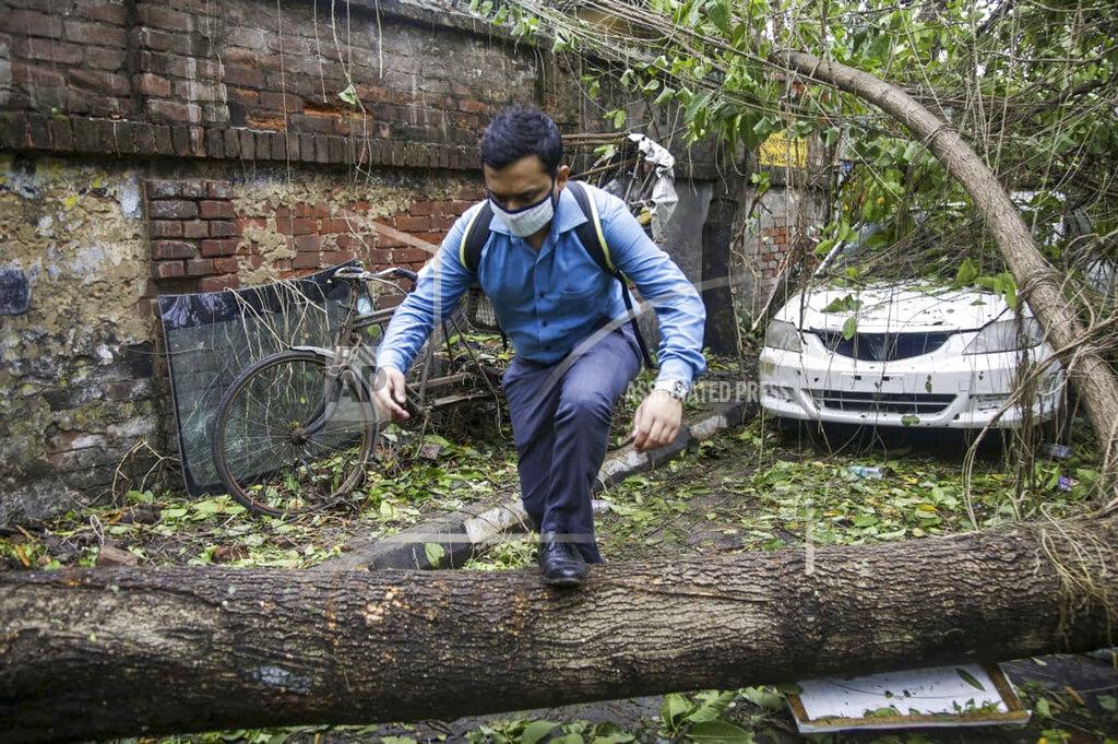 Bikas Das A man makes his way tpast a tree fallen in the middle of a road after Cyclone Amphan hit the region in Kolkata, India, Thursday, May 21, 2020. A powerful cyclone ripped through densely populated coastal India and Bangladesh, blowing off roofs and whipping up waves that swallowed embankments and bridges and left entire villages without access to fresh water, electricity and communications. (AP Photo/Bikas Das)
