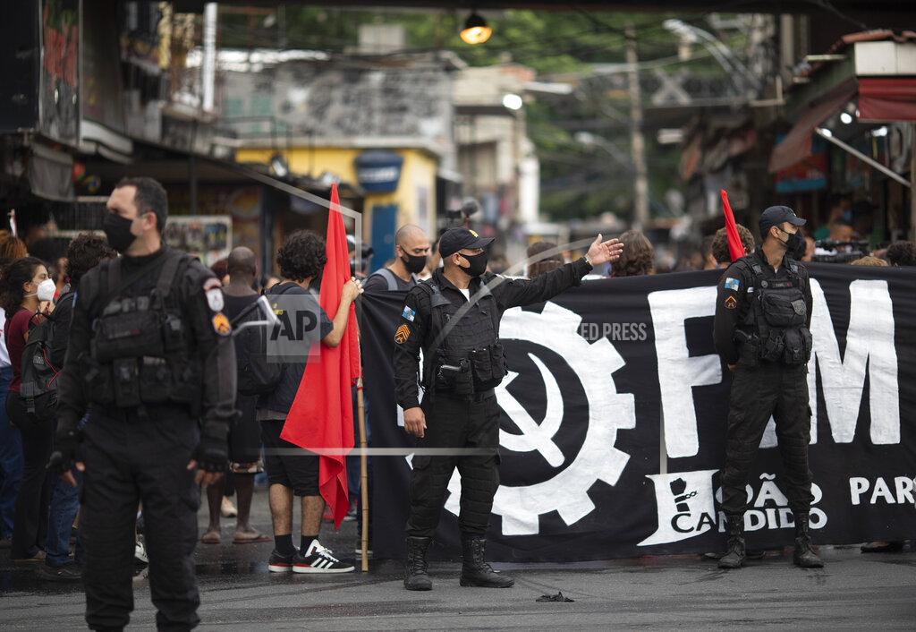 Silvia Izquierdo Police stand guard at the entrance of the Jacarezinho favela as people protest the day after a deadly police operation in the Jacarezinho favela of Rio de Janeiro, Brazil, Friday, May 7, 2021. A bloody, hours-long gunbattle here echoed into Friday, with authorities saying the police mission killed two dozen criminals while residents and activists claimed human rights abuses. (AP Photo/Silvia Izquierdo)
