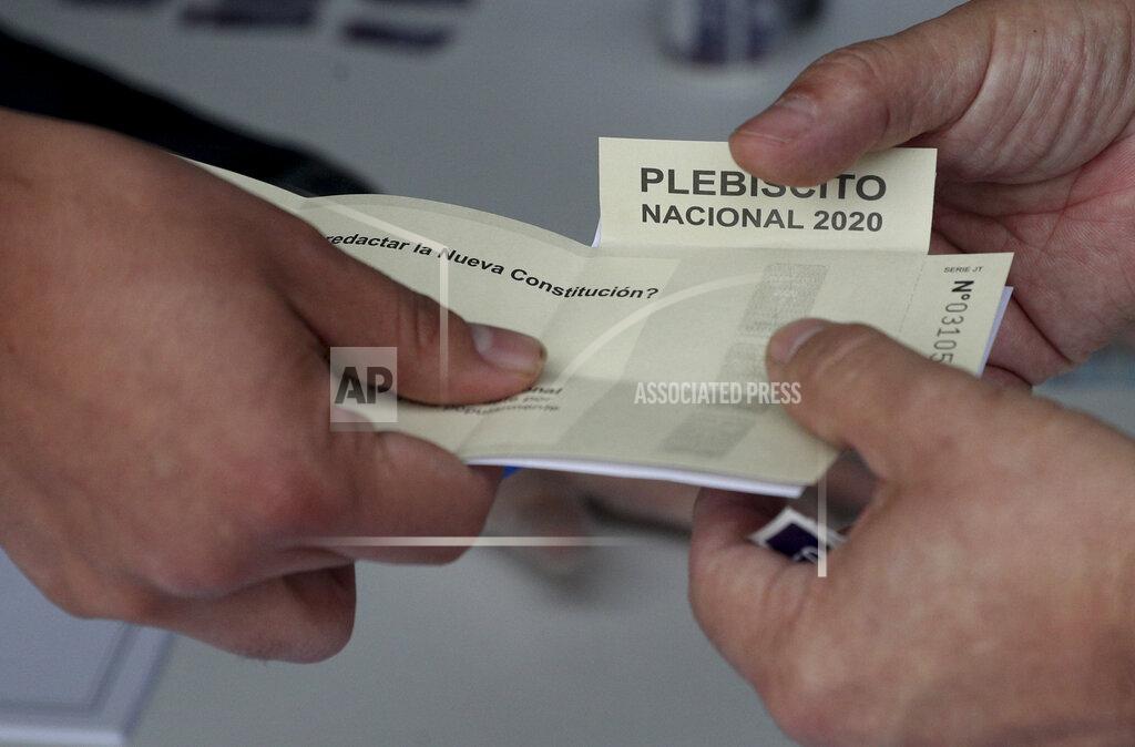 Esteban Felix An electoral official delivers a ballot to a voter at a polling station during a referendum to decide whether the country should replace its 40-year-old constitution, in Santiago, Chile, Sunday, Oct. 25, 2020. (AP Photo/Esteban Felix)