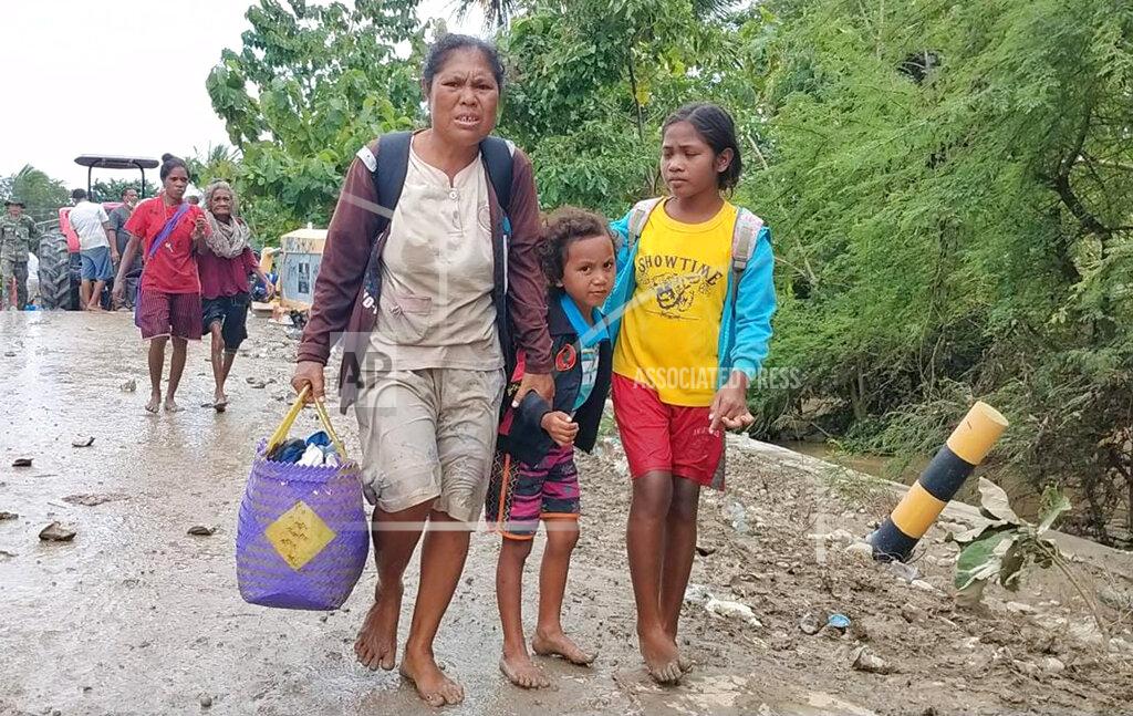 Uncredited A woman with her children carries their belongings as they walk after crossing a flooded road in Malaka Tengah, East Nusa Tenggara province, Indonesia, Monday, April 5, 2021. Multiple disasters caused by torrential rains in eastern Indonesia have left dozens of people dead and missing and displaced thousands, the country's disaster relief agency said Monday. (AP Photo)
