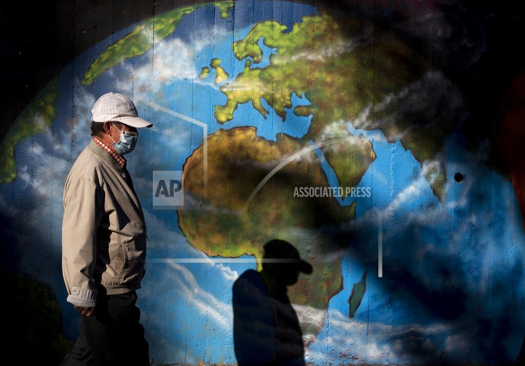 Manu Fernandez FILE - In this Monday, Sept. 28, 2020 file photo, a man wearing a mask walks past graffiti depicting a globe at Orcasitas neighborhood in Madrid, Spain. Public health experts say 1 million worldwide deaths are among reasons to be concerned, if not fearful, of the coronavirus and take everyday precautions despite much rosier advice from the still recovering Donald Trump. (AP Photo/Manu Fernandez)