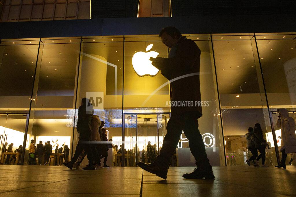 Ng Han Guan FILE - In this Dec. 13, 2019, file photo, a man looks at his phone as he walks past a store of U.S. tech giant Apple in a retail district in Beijing. As Americans celebrate or fume over the new president-elect, many in Asia are waking up to the reality of a Joe Biden administration with decidedly mixed feelings. Relief and hopes of economic and environmental revival jostle with needling anxiety and fears of inattention. The two nations are inexorably entwined, economically and politically, even as the U.S. military presence in the Pacific chafes against China’s expanded effort to have its way in what it sees as its natural sphere of influence. (AP Photo/Ng Han Guan, File)