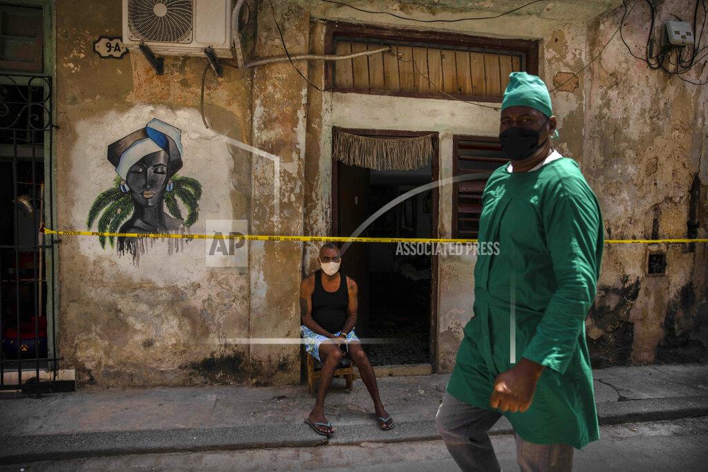 Ramon Espinosa A health worker wearing a mask as a precaution against the spread of the new coronavirus walks in front of a man sitting at the entrance of his quarantined house in Havana, Cuba, Wednesday, April 7, 2021. (AP Photo/Ramon Espinosa)