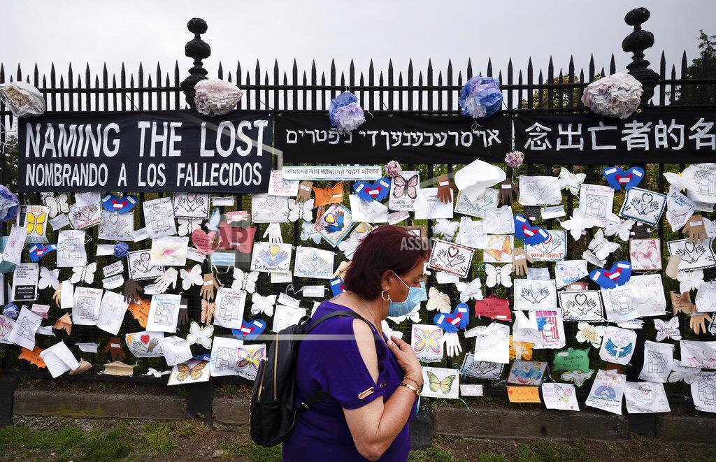 Mark Lennihan FILE - In this May 28, 2020, file photo, a woman passes a fence outside Brooklyn's Green-Wood Cemetery adorned with tributes to victims of COVID-19 in New York. The U.S. death toll from the coronavirus topped 200,000 Tuesday, Sept. 22, a figure unimaginable eight months ago when the scourge first reached the world’s richest nation with its sparkling laboratories, top-flight scientists and towering stockpiles of medicines and emergency supplies. (AP Photo/Mark Lennihan, File)