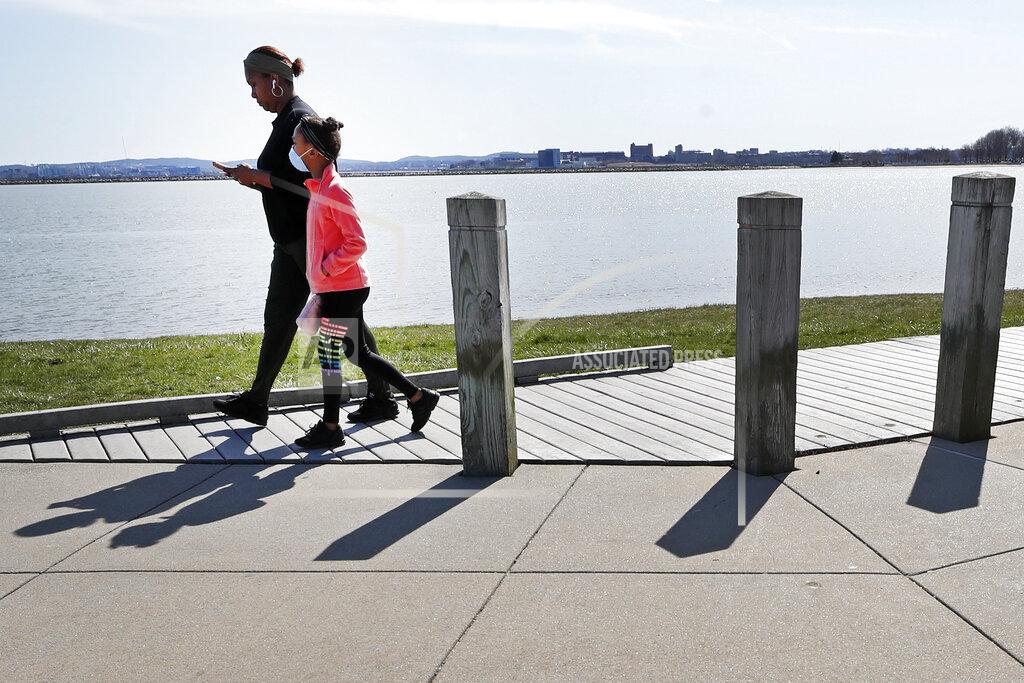 A young girl wears a mask alongside an adult as they walk around Castle Island, Monday, April 6, 2020, in Boston. (AP Photo/Elise Amendola)