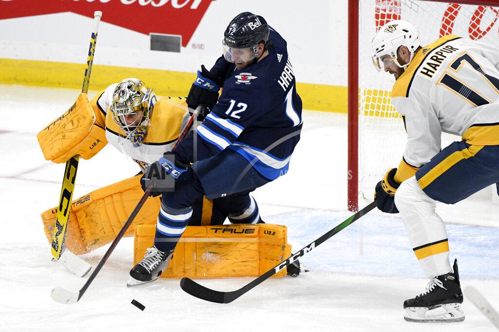Fred Greenslade Winnipeg Jets' Jansen Harkins (12) tries to get the puck in front of Nashville Predators goaltender Juuse Saros (74) and Ben Harpur (17) during the second period of NHL hockey game action in Winnipeg, Manitoba, Saturday, Oct. 23, 2021. (Fred Greenslade/The Canadian Press via AP)