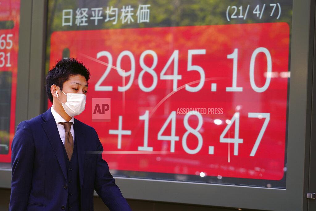 Eugene Hoshiko A man wearing a protective mask walks in front of an electronic stock board showing Japan's Nikkei 225 index at a securities firm Wednesday, April 7, 2021, in Tokyo. Asian shares were mixed Wednesday after Wall Street took a breather, with major indexes edging lower. (AP Photo/Eugene Hoshiko)