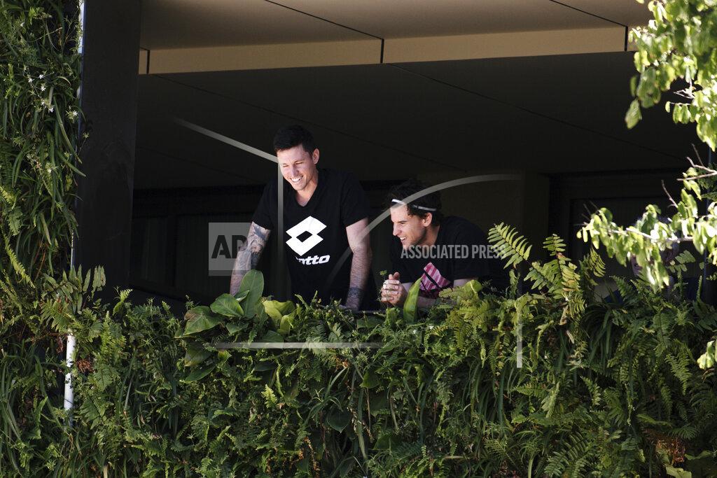Morgan Sette Austria's Dominic Thiem, right, with an unidentified man, stands on the balcony at his accommodation in Adelaide, Australia, Tuesday, Jan. 19, 2021. Australian Open tournament director Craig Tiley defended Serbia's Novak Djokovic for appealing to Australian Open organizers to ease restrictions so players could move to private residences with tennis courts. (Morgan Sette/AAP Image via AP)