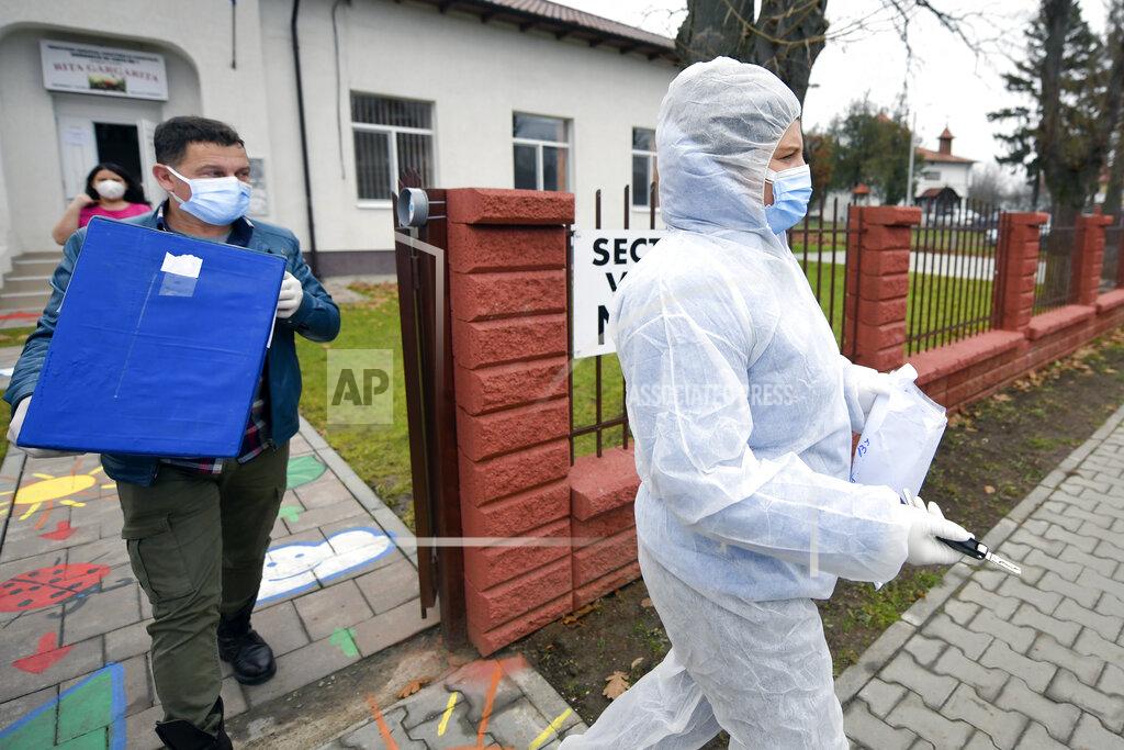 Andreea Alexandru An election official wearing a protective outfit against the COVID-19 infection takes a mobile ballot box to people with mobility issues or quarantined in the village of Branesti, Romania, Sunday, Dec. 6, 2020. Voting started in Romania's legislative election expected to restore some measure of stability after five years of political and social turbulence with more than 18 million Romanians registered to vote for a new legislative body. (AP Photo/Andreea Alexandru)