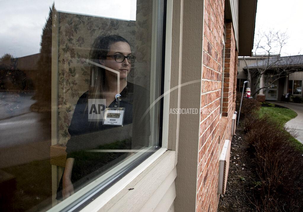 In this Tuesday, March 17, 2020 photo, nurse Alisha Disbennett poses for a photo at a window inside The Inn at Chapel Grove, in Heath, Ohio. Disbennett, along with her fellow staff, have all decided to go on lockdown with the residents, essentially moving into the residence. They made this decision to keep from inadvertently bring the coronavirus into the building and infecting residents who are the most vulnerable population to this virus. Disbennett has two children who are remaining at home in the care of their father. (Jessica Phelps/The Advocate via AP)