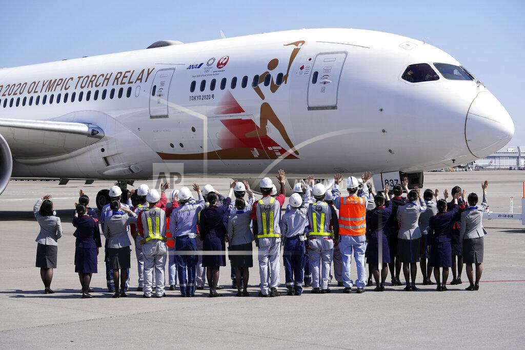 Eugene Hoshiko Ground crews of Japanese airlines wave to the special "Tokyo 2020 Go" aircraft that will transport the Olympic Flame to Japan after the Torch Handover Ceremony in Greece, on its departure at Haneda International Airport in Tokyo Wednesday, March 18, 2020. (AP Photo/Eugene Hoshiko)
