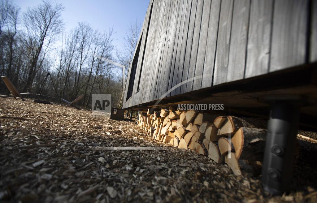 Virginia Mayo Two chairs are placed next to a fire pit and wood is stacked under a Slow Cabin awaiting a visitor in Zandbergen, Belgium, Sunday, Feb. 28, 2021. These Slow Cabins, set up the Belgian countryside, are the new way to vacation in pandemic times: in complete solitude and in the middle of nowhere. The wooden cabins are fully sustainable, provided you don't stay in the shower too long and you can live without Wi-Fi. (AP Photo/Virginia Mayo)