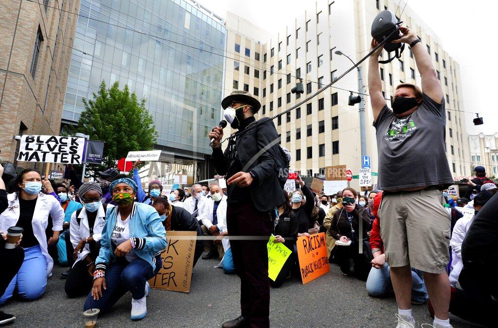 Alan Berner With a speaker held aloft to reach the back of the crowd, Edwin Lindo, center, addresses protesters gathered outside Harborview Medical Center and kneeling to honor George Floyd in Seattle, Saturday, June 6, 2020. Floyd died after being restrained by Minneapolis police officers on May 25. (Alan Berner/The Seattle Times via AP)