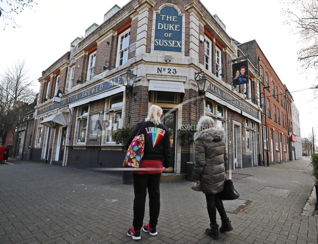 Frank Augstein People stop to look at a sign depicting the image of Britain's Prince Harry and his wife Meghan, which hangs outside the Duke of Sussex pub near Waterloo station, London, Tuesday March 9, 2021. Prince Harry and Meghan's explosive TV interview has divided people around the world, rocking an institution that is struggling to modernize with claims of racism and callousness toward a woman struggling with suicidal thoughts. (AP Photo/Frank Augstein)