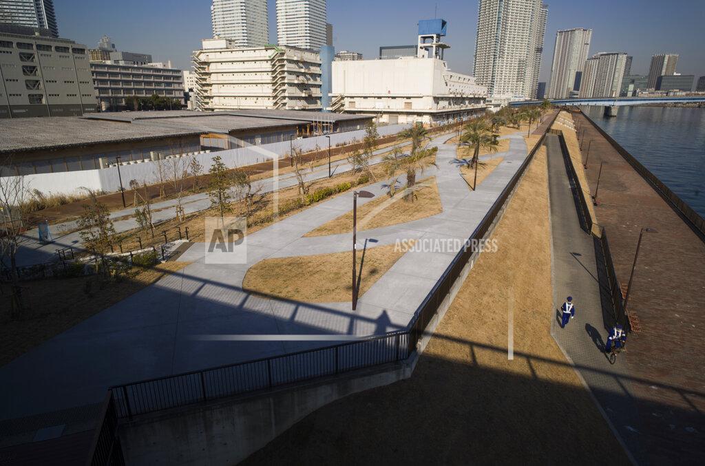 Hiro Komae Security guards, bottom right, pass by each other as they patrol the closed area of the riverbank adjacent to a closed building complex, back left, built to be used for the athletes' village during the rescheduled Tokyo Olympics, in Tokyo on Thursday, Jan. 21, 2021. The postponed Tokyo Olympics are to open in just six months. Local organizers and the International Olympic Committee say they will go ahead on July 23. But it’s still unclear how this will happen with virus cases surging in Tokyo and elsewhere around the globe. (AP Photo/Hiro Komae)