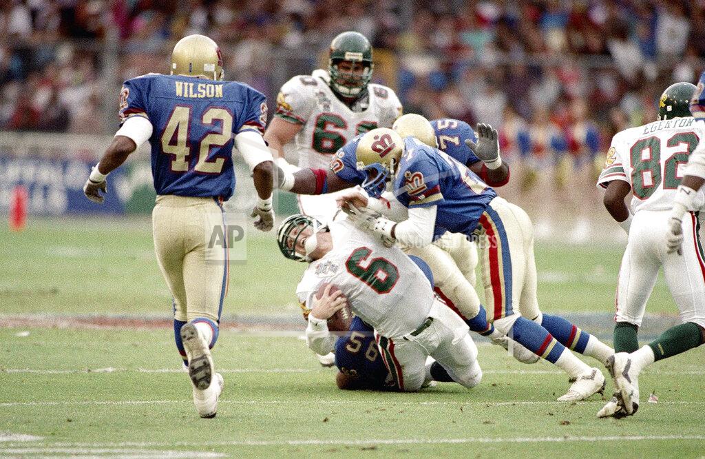 Mike Feldman FILE - In this file photo dated June 9, 1991, Barcelona Dragons quarterback Scott Erney (6), is pulled to the ground after he was sacked by London Monarchs' Corris Ervin, right, and Roy Hart (75) in the second quarter of action in their World League Football Championship, World Bowl, game in London. The 2021 year marks the 30th anniversary of the World League of American Football. (AP Photo/Mike Feldman, FILE)