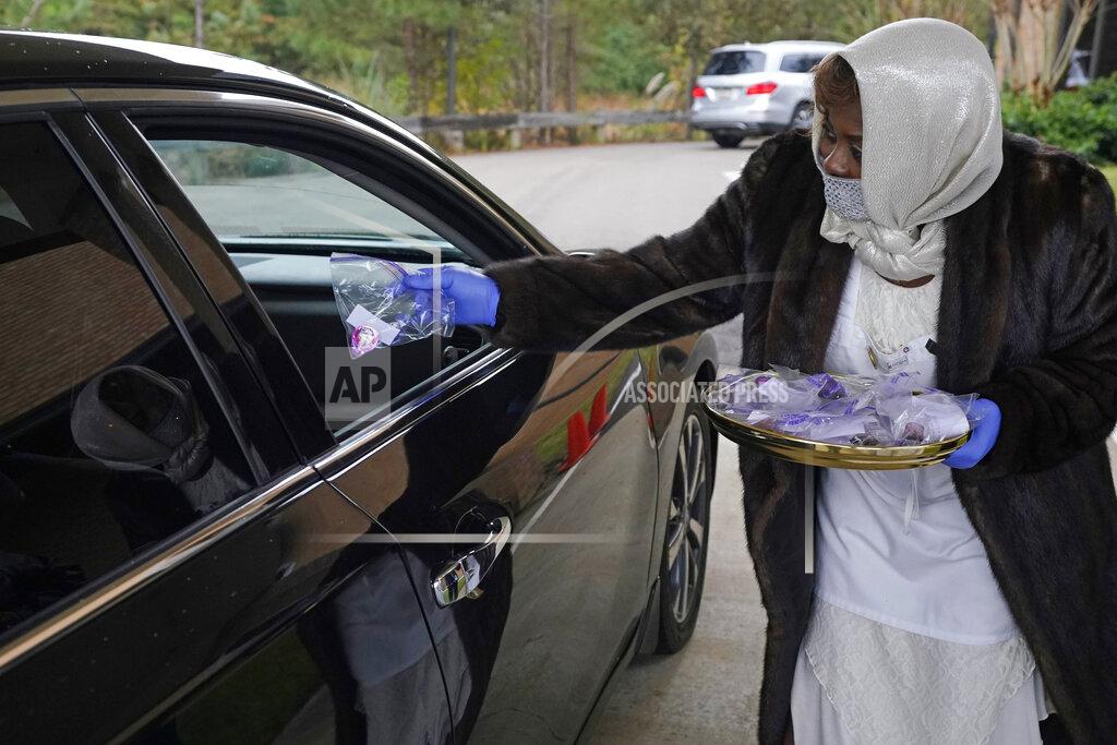 Usher Gloria Addison hands out a communion packet and radio frequency notice to a church member prior to the start of a First Sunday service at Anderson United Methodist Church, Dec. 6, 2020, in Jackson, Miss. The church has taken to using a variety of digital means by which to broadcast the majority of its church services to the members. However, for First Sunday services, the congregants gather in the church's parking lot to celebrate the receiving of communion in their personal vehicles. (AP Photo/Rogelio V. Solis)