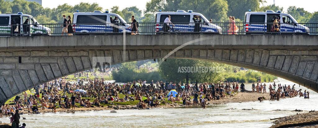 Peter Kneffel Police cars stand on a bridge next to hundreds of people staying at the banks of the river Isar after ongoing relaxing of measures against the coronavirus outbreak in Munich, Germany, Saturday, June 13, 2020. (Peter Kneffel/dpa via AP)