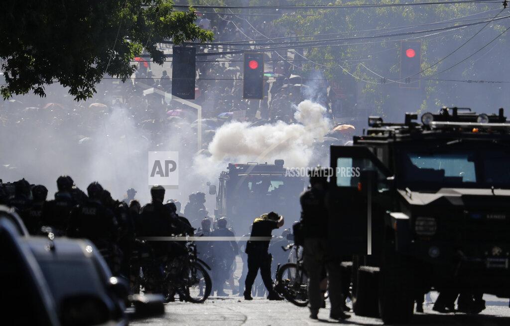Ted S. Warren FILE - In this July 25, 2020, file photo, smoke rises as police clash with protester during a Black Lives Matter protest near the Seattle Police East Precinct headquarters in Seattle. A Seattle police officer who threw a tear gas canister that hit a reporter and other officers who threw blast balls that hit individuals during last summer's Black Lives Matter protests violated policies, according to new reports from an independent agency tasked with investigating police misconduct. The agency has released five batches of investigative reports since September, with the latest 22 cases posted Friday, Jan. 15, 2021. (AP Photo/Ted S. Warren, File)