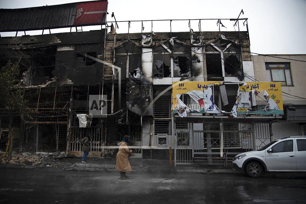 In this photo taken Monday, Nov. 18, 2019, and released by Iranian Students' News Agency, ISNA, people walk past buildings which burned during protests that followed the authorities' decision to raise gasoline prices, in the city of Karaj, west of the capital Tehran, Iran. An article published Tuesday in the Keyhan hard-line newspaper in Iran is suggesting that those who led violent protests will be executed by hanging as the unrest continues. (Masoume Aliakbar/ISNA via AP)