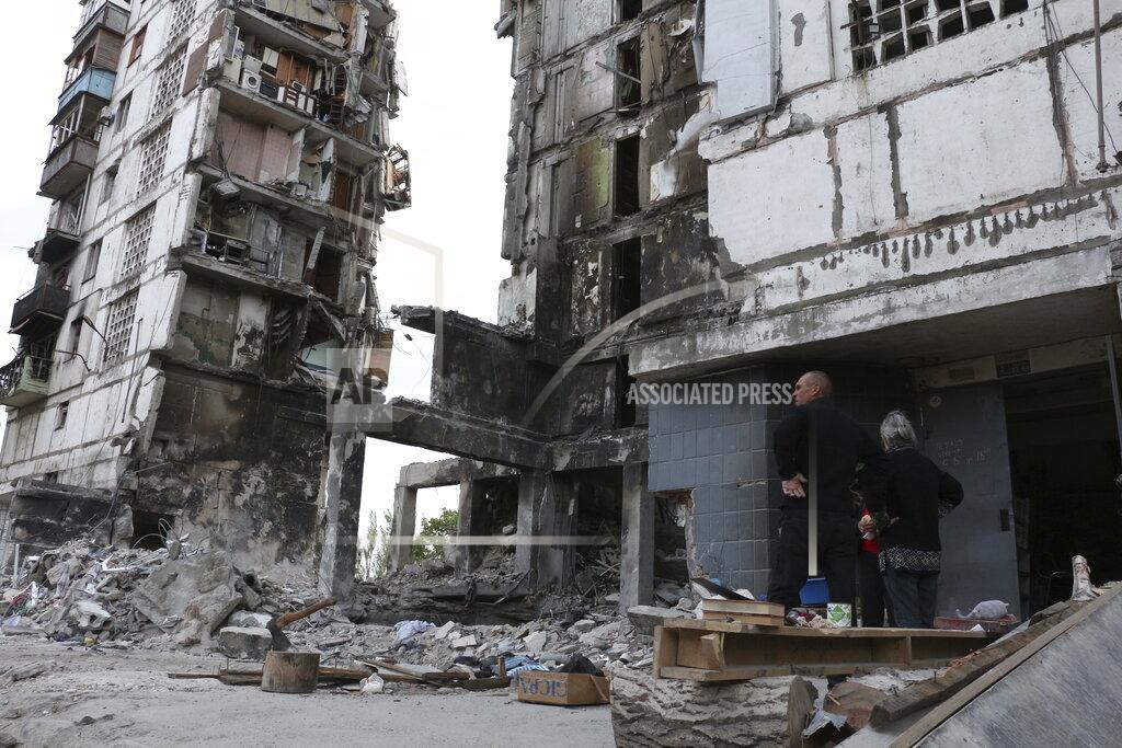 Uncredited Local residents stand at the side of damaged during a heavy fighting buildings in Mariupol, in territory under the government of the Donetsk People's Republic, eastern Ukraine, Friday, May 13, 2022. (AP Photo)