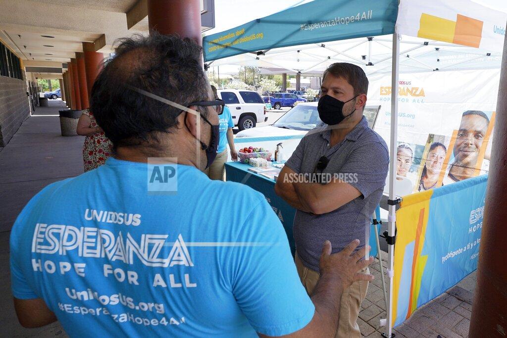 Arizona Democrat Rep. Ruben Gallego, right, talks with Jose Marquez, left, of UnidosUS, at an informational tent set up to increase efforts to bring more vaccine doses into Latino neighborhoods at a local shopping plaza Friday, May 7, 2021, in Phoenix. Gallego said he is helping organize vaccination events in Latino neighborhoods, including one May 15 at a west Phoenix high school. (AP Photo/Ross D. Franklin)