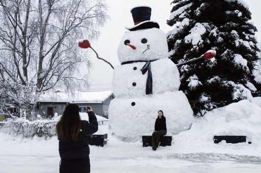 FILE - Isil Mico takes a photo of her sister-in-law Oznur Mico in front of Snowzilla, a snowman measuring more than 20 feet tall, in Anchorage, Alaska on Jan. 10, 2024. A recent storm dropped nearly 16 inches of snow on Anchorage, bringing the seasonal total to over 103 inches. It&rsquo;s the earliest Alaska&rsquo;s largest city has reached the 100-inch mark. (AP Photo/Mark Thiessen, File)
