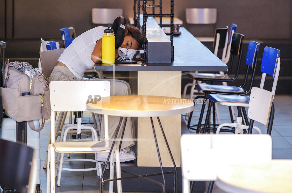 Olivier Matthys FILE - A woman sleeps on a charging station table in the departures hall at Brussels international airport during a general strike in Brussels, Monday, June 20, 2022. (AP Photo/Olivier Matthys, File)