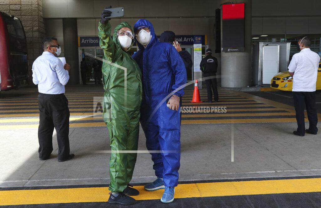 Dolores Ochoa A couple decked out in full protection suits and wearing masks against the spread of the new coronavirus, take a selfie while waiting for the arrival of their son in one of the firsts international flights from United States, outside the Mariscal Sucre airport, in Quito, Ecuador, Thursday, June 4, 2020. The airport's waiting area was closed to prevent agglomerations amid the COVID-19 pandemic. (AP Photo/Dolores Ochoa)