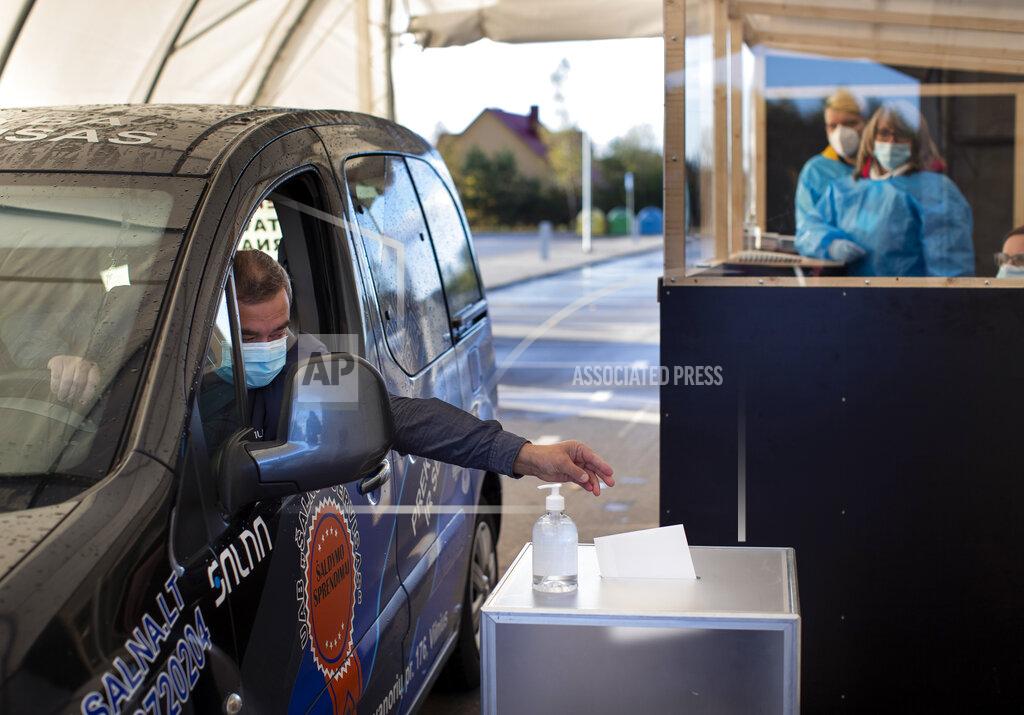 Mindaugas Kulbis A voter, wearing face masks to protect against coronavirus casts his ballot on the first day of early voting in the second round of a parliamentary election at a drive-in polling station, special place of advance voting for self isolated voters in Vilnius, Lithuania, Monday, Oct. 19, 2020. Lithuanians are voting in the second round of a parliamentary election on Sunday during the rise in the incidence of coronavirus infection in the country. (AP Photo / Mindaugas Kulbis)