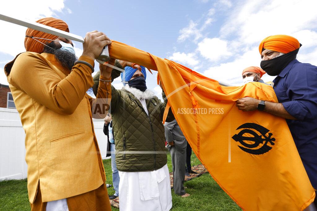 Jasbir Singh, left, and Harvinder Singh, right, assist head priest Gaini Kuldeep Singh, center, with a ceremonial changing of the Sikh flag during Vaisakhi celebrations at Guru Nanak Darbar of Long Island, Tuesday, April 13, 2021 in Hicksville, N.Y. Sikhs across the United States are holding toned-down Vaisakhi celebrations this week, joining people of other faiths in observing major holidays cautiously this spring as COVID-19 keeps an uneven hold on the country. (AP Photo/Jason DeCrow)