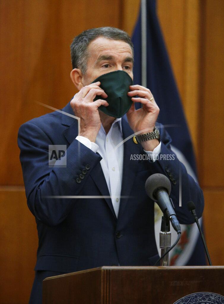 Virginia Gov. Ralph Northam demonstrates how to wear a face mask to help prevent the spread of the coronavirus as he addresses his daily news briefing inside the Patrick Henry Building in Richmond, Va., Monday, April 6, 2020. He said that the mask was made by inmates at one of Virginia's penal facilities. (Bob Brown/Richmond Times-Dispatch via AP)