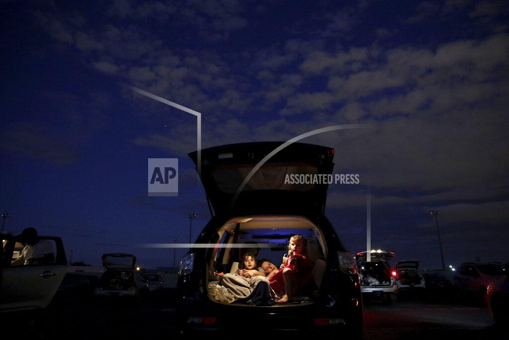 A family watches a movie from the back of their car at a drive-in movie theater where drivers must leave one space empty between them amid the new coronavirus pandemic in Brasilia, Brazil, Saturday, May 23, 2020. The drive-in is 47 years old and one of the only such open-air facilities in operation in Brazil. (AP Photo/Eraldo Peres)