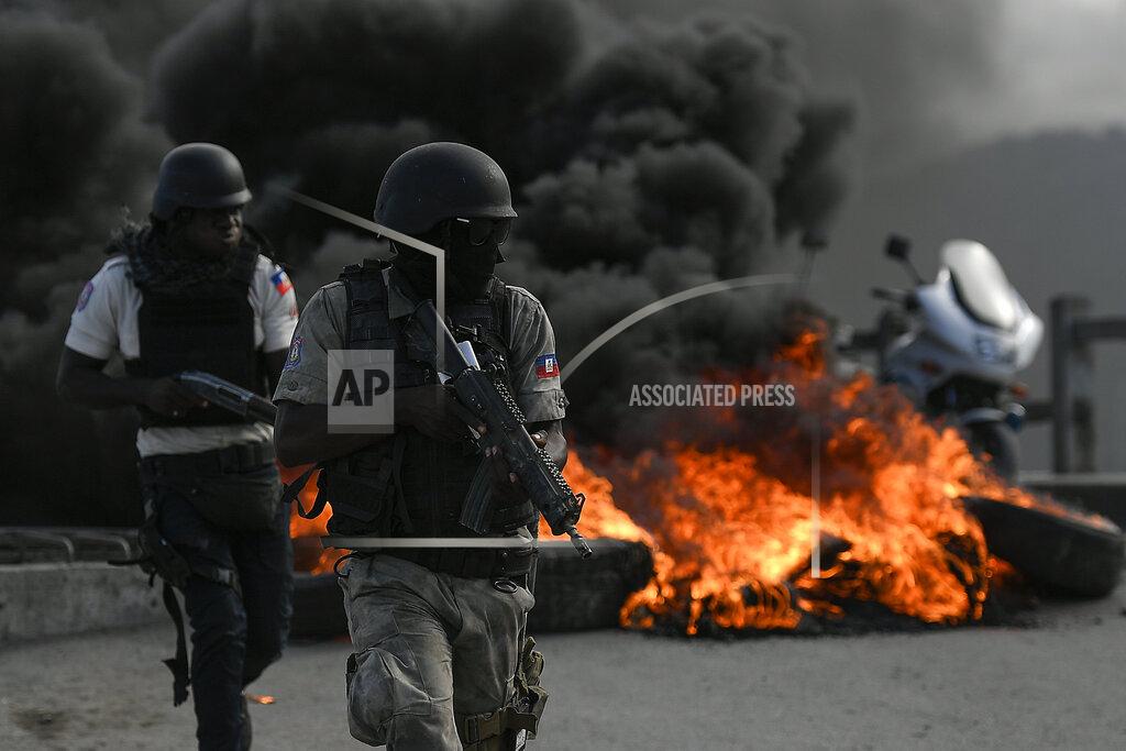 Matias Delacroix Armed police take cover near a barricade set on fire by protesters demanding justice for the assassinated President Jovenel Moise stands, in Cap-Haitien, Haiti, Thursday, July 22, 2021. Demonstrations after a memorial service for Moise turned violent on Thursday afternoon with protesters shooting into the air, throwing rocks and overturning heavy concrete barricades next to the seashore as businesses closed and people took cover. (AP Photo/Matias Delacroix)