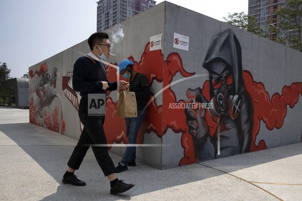 Ng Han Guan A man lowers his mask to smoke as he walks past graffiti artwork in Beijing Monday, July 13, 2020. China reported eight new cases, all of them brought from outside the country, as domestic community infections fall to near zero (AP Photo/Ng Han Guan)