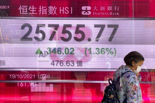 A woman walks past a bank's electronic board showing Hong Kong's Hang Seng share index in Hong Kong Tuesday, Oct. 19, 2021. Asian stock markets followed Wall Street higher as investors waited Tuesday for U.S. corporate results to see how companies are coping with supply disruptions and the past quarter's surge in coronavirus infections. (AP Photo/Vincent Yu)
