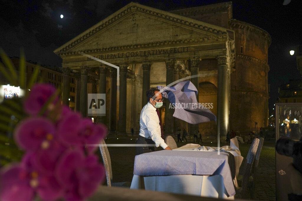 Andrew Medichini A waiter clears a table before closing a restaurant in front of the Pantheon, Rome, Monday, Oct. 26, 2020. For at least the next month, people outdoors except for small children must now wear masks in all of Italy, gyms, cinemas and movie theaters will be closed, ski slopes are off-limits to all but competitive skiers and cafes and restaurants must shut down in early evenings, under a decree signed on Sunday by Italian Premier Giuseppe Conte, who ruled against another severe lockdown despite a current surge in COVID-19 infections. (AP Photo/Andrew Medichini)