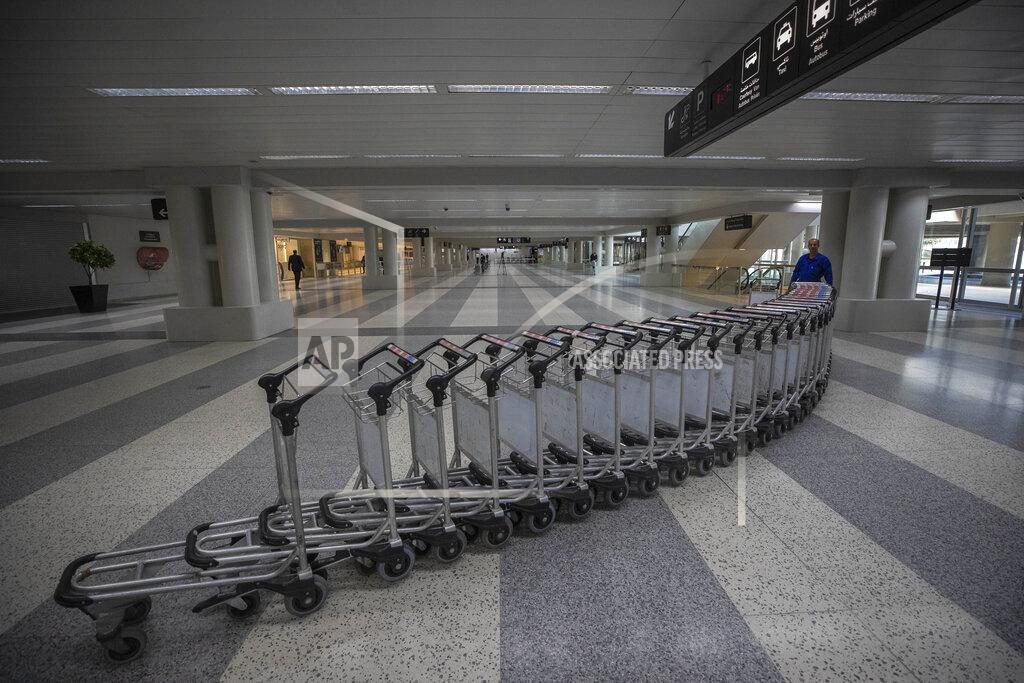Hassan Ammar FILE - In this March 19, 2020 file photo, a worker pushes trollies at an empty terminal hall of the Rafik Hariri International Airport, in Beirut, Lebanon. On Wednesday, July 1, 2020, Beirut's airport is partially reopening after a three-month shutdown and Lebanon's cash-strapped government hopes thousands of Lebanese expatriates will return for the summer, injecting badly needed dollars into the sinking economy. (AP Photo/Hassan Ammar, File)