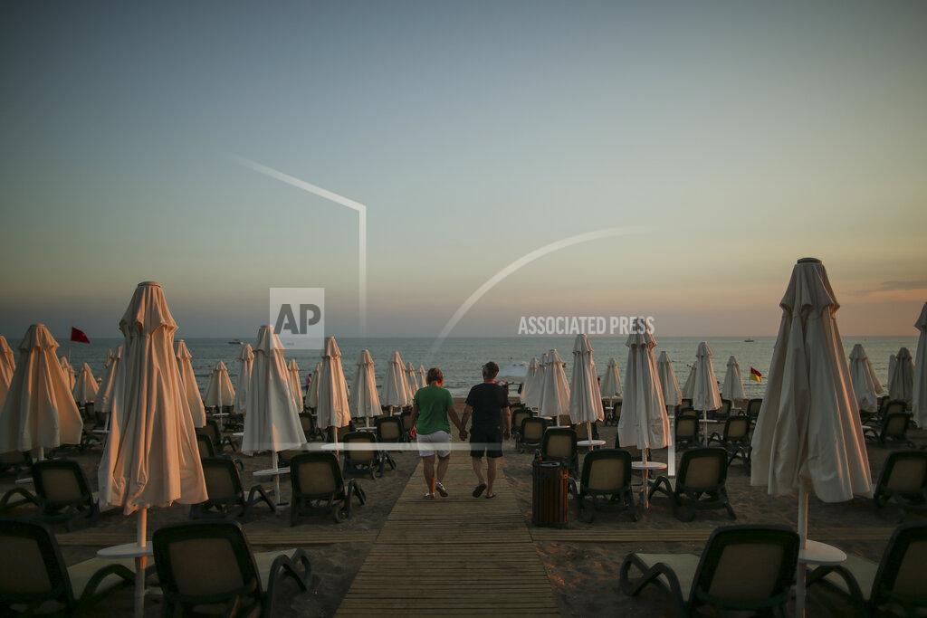Emrah Gurel Tourists walk at the beach of Antalya, southern Turkey, as the sun sets, on Sunday, June 20, 2021. Hotels in Turkey's Antalya region, a destination beloved by holidaymakers, are preparing to finally resume operations as they expect the return of international tourists after months of setbacks caused by the pandemic that halted travel. (AP Photo/Emrah Gurel)
