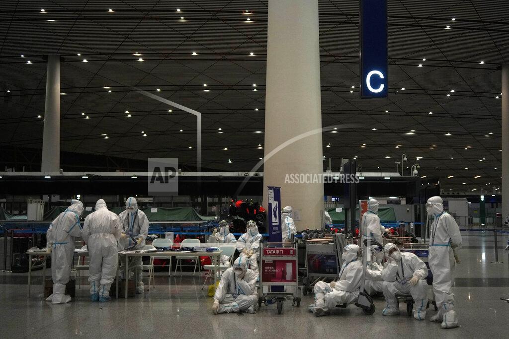 Olympic workers in protective clothing rest after they helped travelers at Beijing Capital International airport after the 2022 Winter Olympics, Monday, Feb. 21, 2022, in Beijing, China. (AP Photo/Alessandra Tarantino)