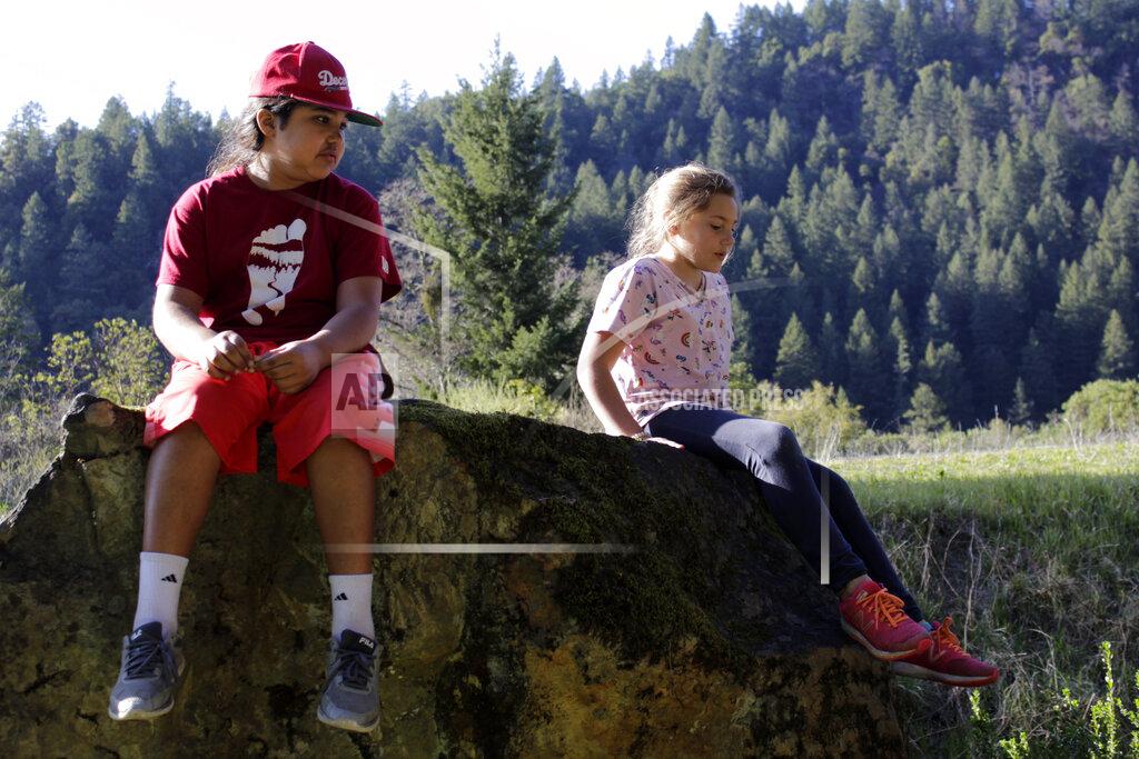 Gillian Flaccus Ishikiihara E-kor plays with his younger sister, Vuunsip Imkuukirii, on rocks near the Karuk Tribal Administration headquarters in the unincorporated community of Orleans in Humboldt County, Calif., on March 4, 2020. Ishikiihara, whose name means sturgeon warrior in the Karuk language, is one of 5,000 members of the Karuk tribe still living in a remote area of far northern California. Ishikiihara has been doing distance learning and has been coping with the pandemic by writing rap songs, one of his favorite hobbies. He celebrated his recent 11th birthday with relatives on a video conference call. (AP Photo/Gillian Flaccus)