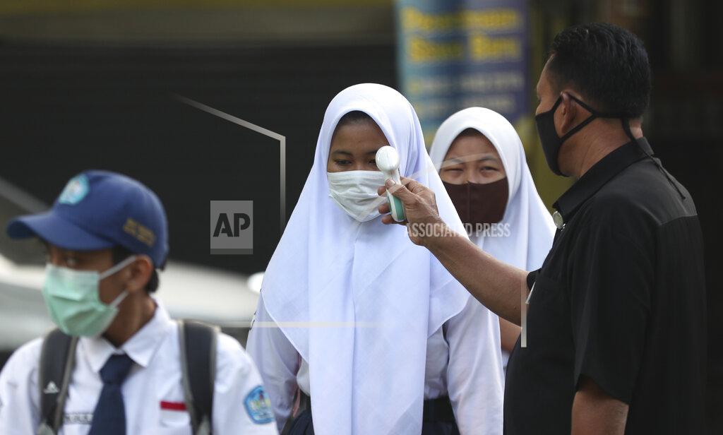 Achmad Ibrahim A security guard checks the body temperature of a student before entering a school amid coronavirus outbreak during the first day of school reopening at a state high school in Bekasi on the outskirts of Jakarta, Indonesia July 13, 2020. (AP Photo/Achmad Ibrahim)