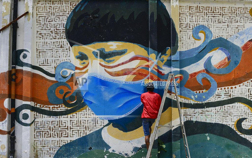 Matias Delacroix A street artist spray paints a protective face mask over an old mural featuring a Venezuelan Indigenous man, in Caracas, Venezuela, Saturday, July 18, 2020, amid the new coronavirus pandemic. (AP Photo/Matias Delacroix)