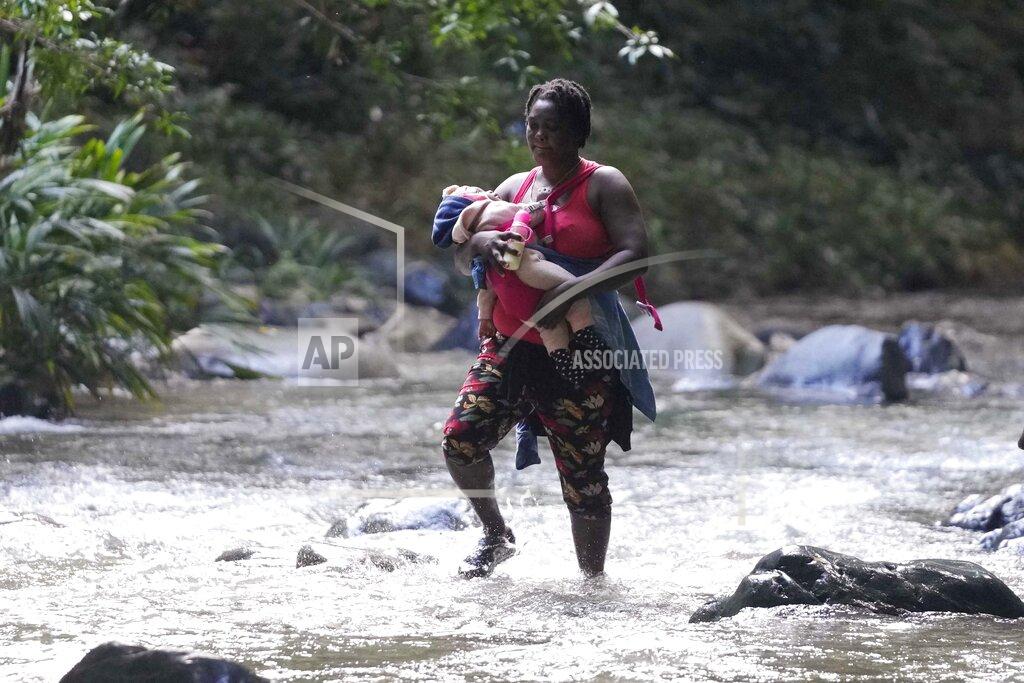 Fernando Vergara A migrant woman crosses the Acandi River with a child in her arms, in Acandi, Colombia, Wednesday, Sept. 15, 2021. A group of migrants, following a well-beaten, multi-nation journey towards the U.S., will continue their journey through a jungle known as the Darien Gap. (AP Photo/Fernando Vergara)