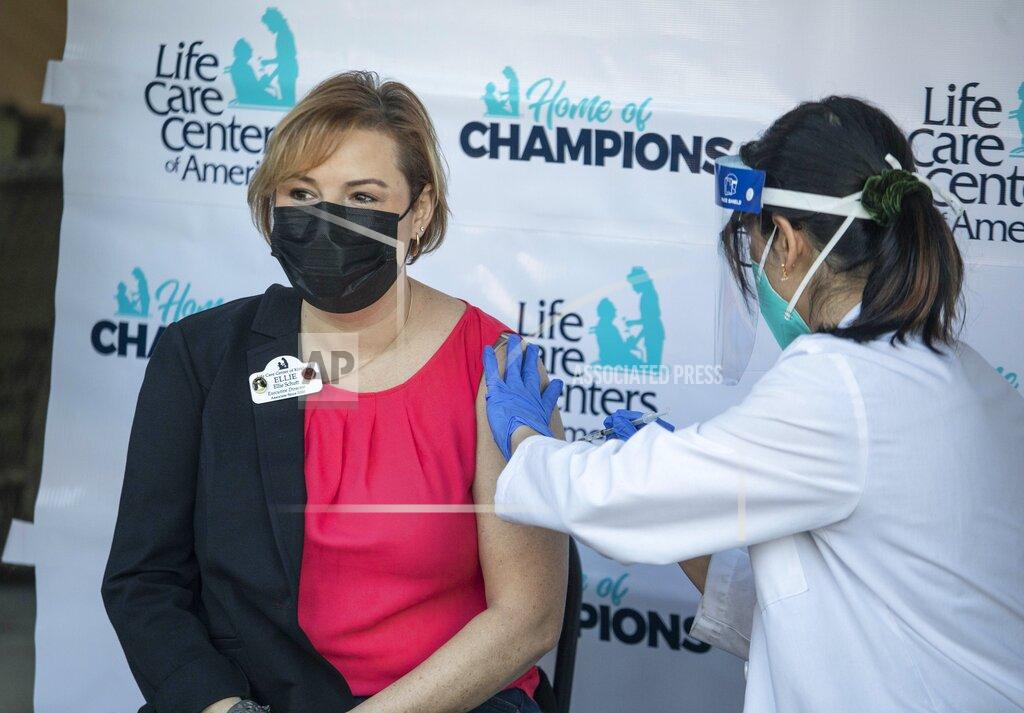 Steve Ringman Ellie Basham, Executive Director at Life Care Center in Kirkland, Wash., being vaccinated by Kristine Kim, a pharmacist for CVS outside the Center in Kirkland, Wash., Monday, Dec. 28, 2020. (Steve Ringman/The Seattle Times via AP)