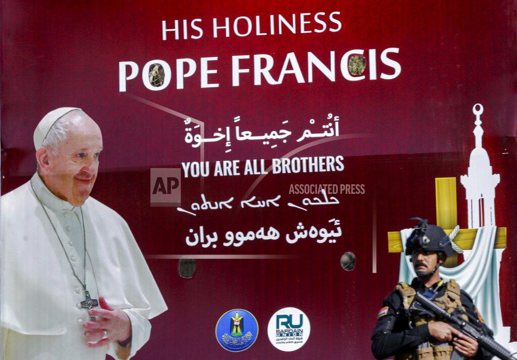 Andrew Medichini Iraqi security stand by a poster depicting Pope Francis, in Baghdad Iraq, Friday, March 5, 2021. Pope Francis heads to Iraq on Friday to urge the country's dwindling number of Christians to stay put and help rebuild the country after years of war and persecution, brushing aside the coronavirus pandemic and security concerns. (AP Photo/Andrew Medichini)