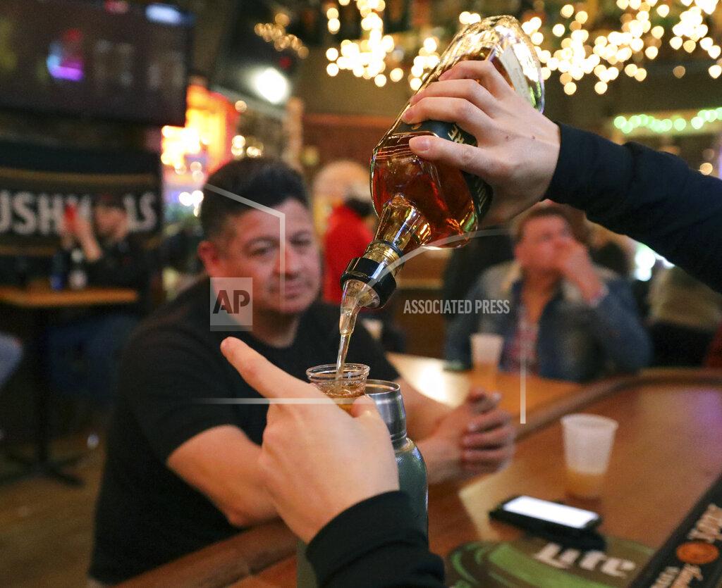 Shafkat Anowar A waiter of Lottie's Pub pours alcohol into a shot glass as Frank Robelli, left, and Cliff Naumann watch Saturday, March 13, 2021, in Chicago's Bucktown neighborhood. The NCAA Tournament and bars were made for each other. This year, the tournament’s back, and bars and restaurants, some shuttered for months, are open for March Madness, though things may look a little different. (AP Photo/Shafkat Anowar)